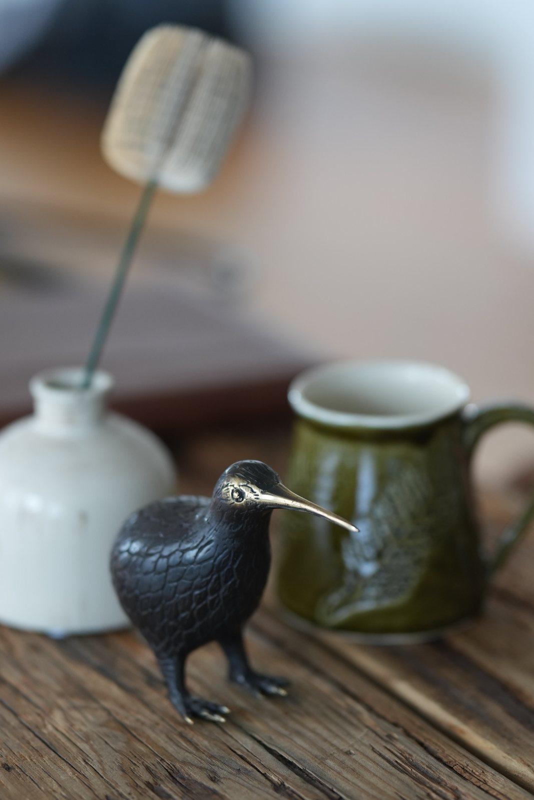 A small bronze kiwi beside a green mug