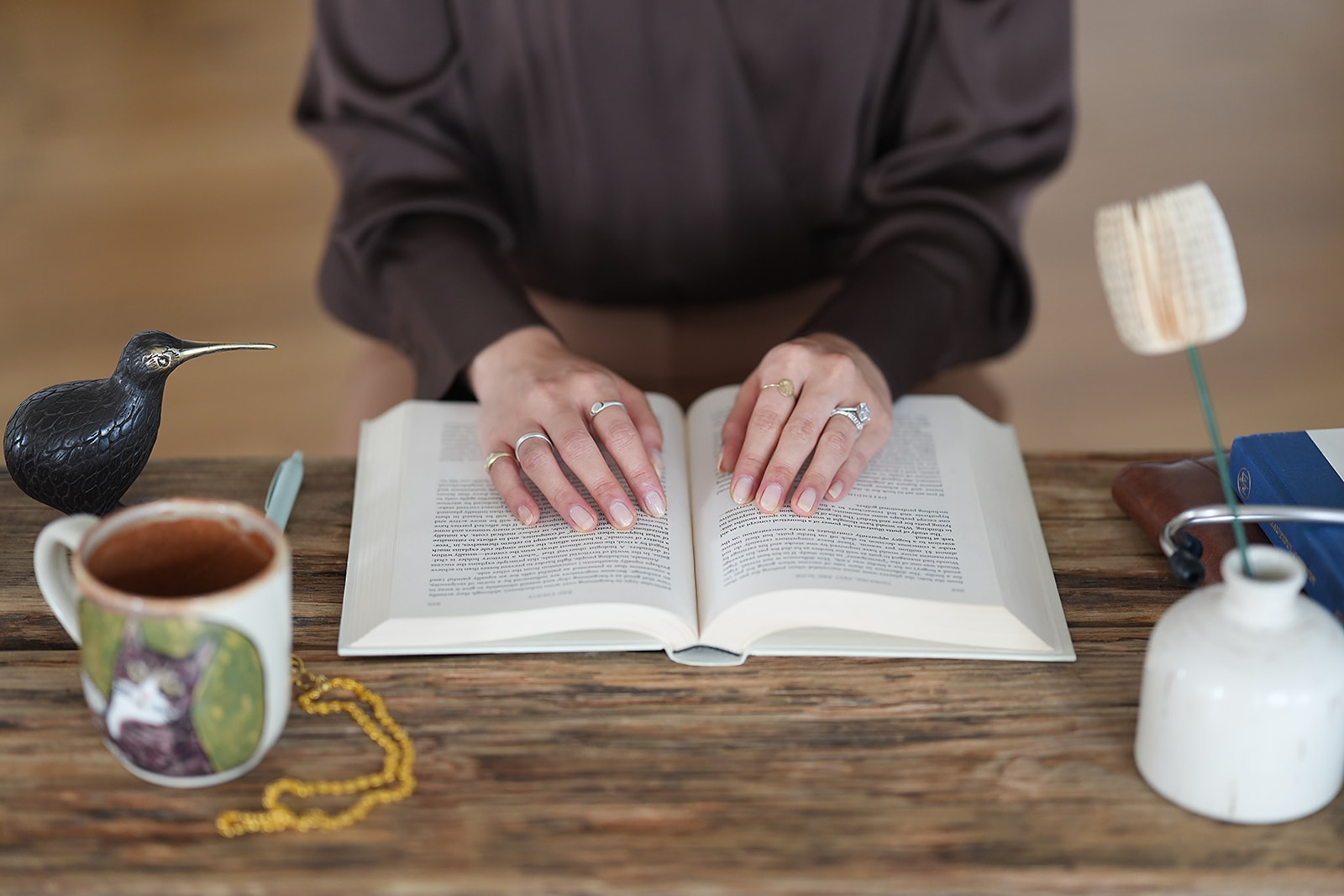 Hands resting open on a book at a wooden table